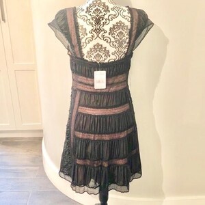 May include: Black dress with a tiered skirt and lace trim. The dress features a scoop neckline and cap sleeves. The bodice has horizontal bands of lace. A tag hangs from the dress.