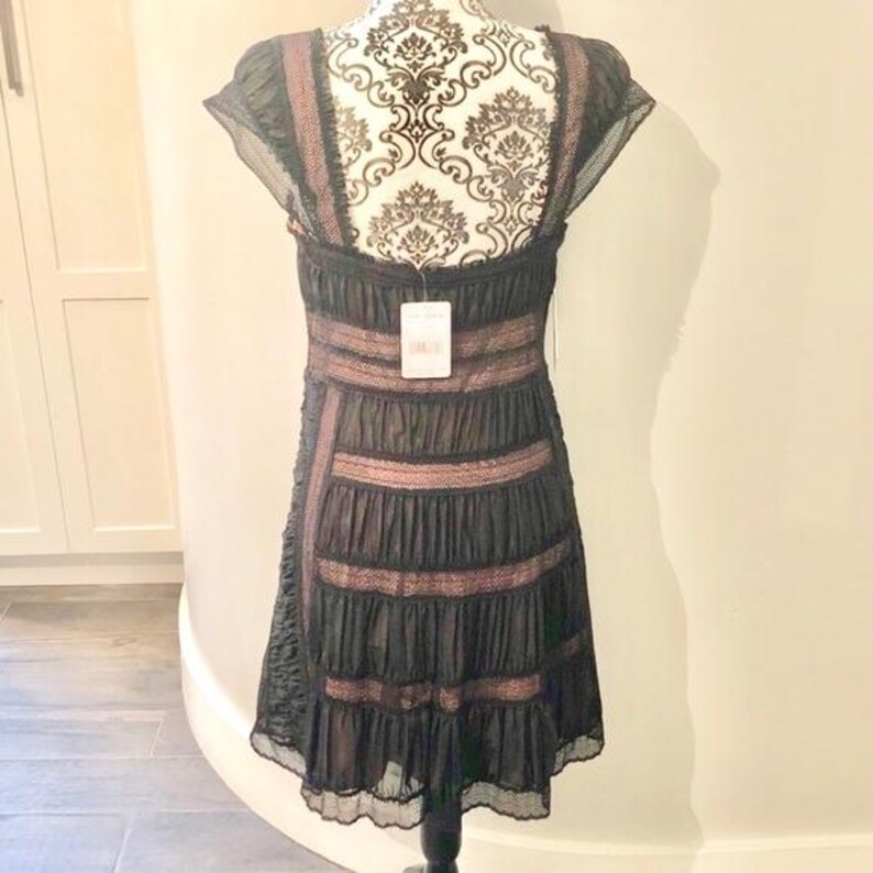 May include: Black dress with a tiered skirt and lace trim. The dress features a scoop neckline and cap sleeves. The bodice has horizontal bands of lace. A tag hangs from the dress.