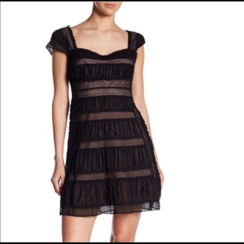 May include: Black mini dress with a sweetheart neckline, short sleeves, and a tiered skirt. The dress features a sheer, layered design with a fitted bodice and a flared skirt. The dress is made of a lightweight fabric.