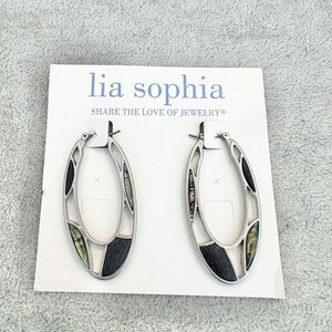 May include: A pair of oval hoop earrings with silver-tone metal frames. The earrings feature black, white, and iridescent abalone shell inlays. The earrings are displayed on a white card with the text "lia sophia SHARE THE LOVE OF JEWELRY®".