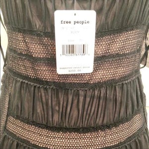 May include: Close-up of a black dress with a layered design. The dress features a lace and sheer fabric construction. A white tag from "free people" is attached, with the size and color information.