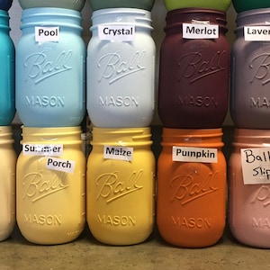 May include: A collection of 12 painted mason jars with various colors and names, including Agave, Lagoon, Pool, Crystal, Merlot, Lavender, English Lavender, White, Cashew, Summer Porch, Maize, Pumpkin, Ballet Slipper, and Rhubarb. The Rhubarb jar is marked "Sold Out".