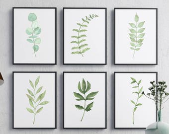 May include: Set of six black framed prints featuring watercolor illustrations of various green leaves and branches. The prints are arranged in a grid pattern on a white wall.
