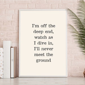 May include: A white framed print with a black and white text quote that reads "I'm off the deep end, watch as I dive in, I'll never meet the ground". The print is displayed on a white brick wall with a potted plant and books on a shelf.