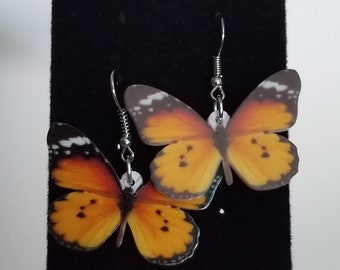 May include: A pair of butterfly earrings with orange, black, and white wings. The earrings are made of metal and have a hook closure.