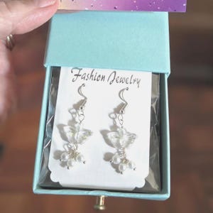 May include: A pair of fashion earrings with a butterfly design and small white pearls, displayed in a light blue gift box. The earrings are on a card that reads "Fashion Jewelry".