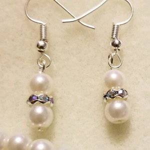 May include: A pair of silver earrings with two white pearls and a band of iridescent rhinestones on each earring.