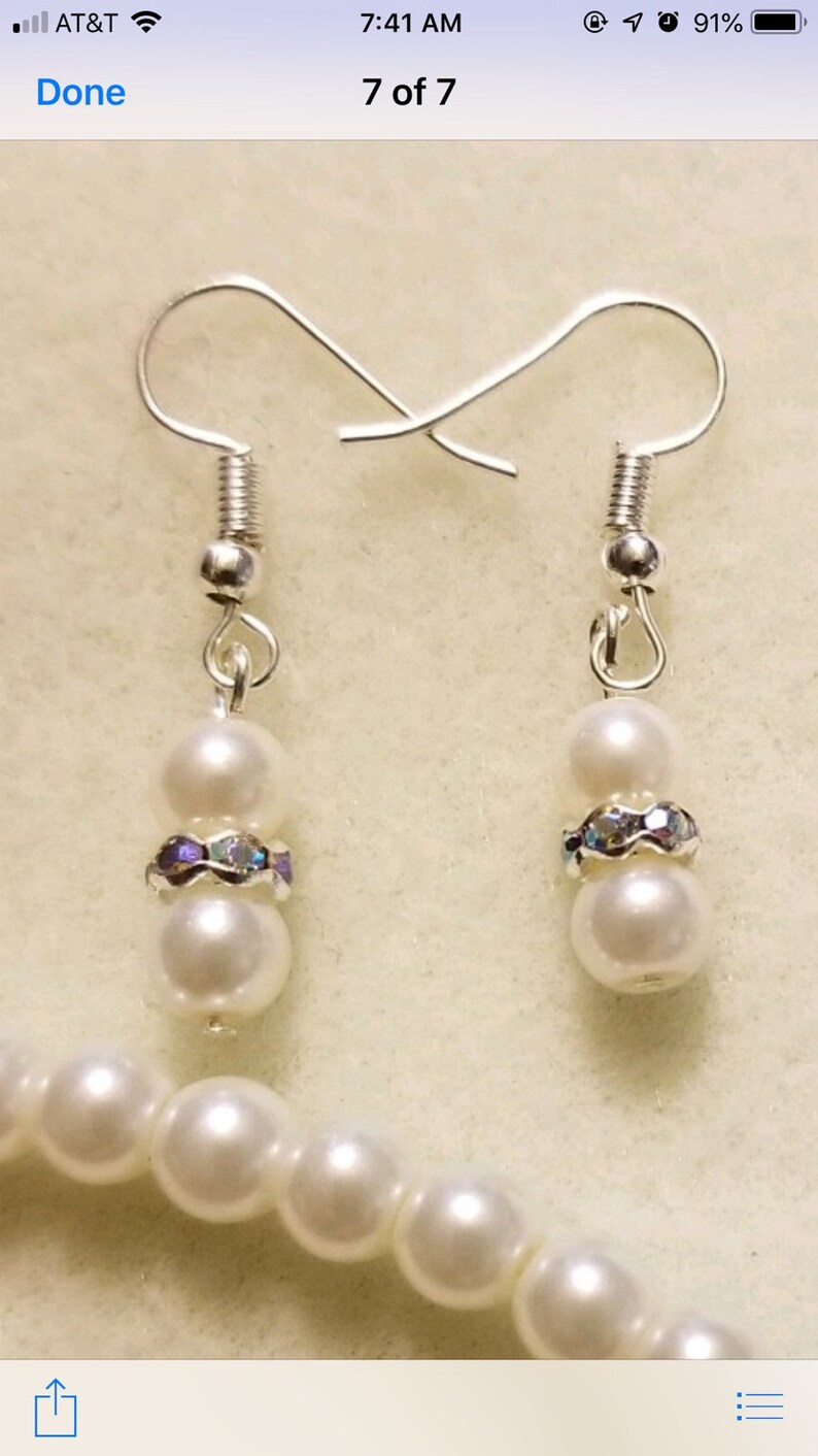 May include: A pair of silver earrings with two white pearls and a band of iridescent rhinestones on each earring.