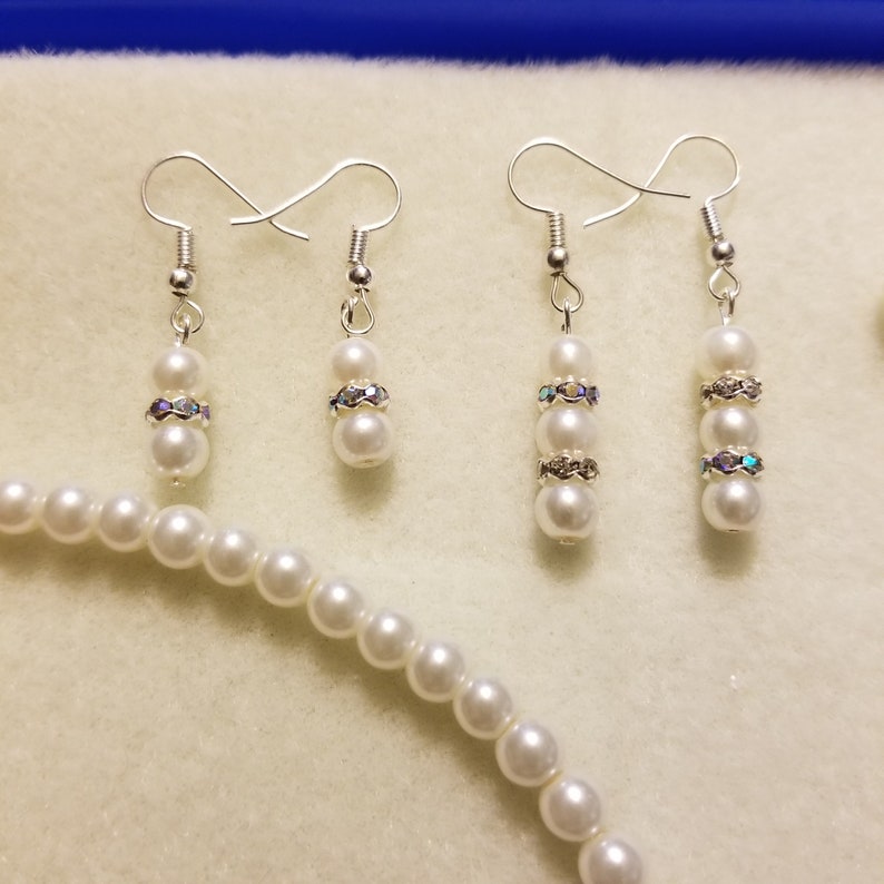 May include: A set of pearl earrings and a pearl necklace. The earrings have three pearls each with a rhinestone accent. The necklace is a strand of white pearls.