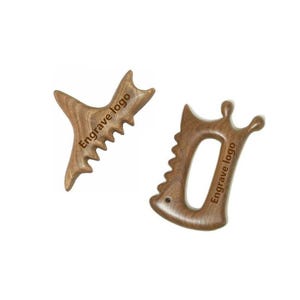 May include: Two wooden massage tools. One is Y-shaped with a serrated edge, the other is a curved shape with a handle and a similar serrated edge. Both have the text "Engrave logo" and are light brown.