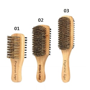 Op de afbeelding: Drie houten haarborstels met natuurlijke borstels. De borstels hebben een dubbelzijdig ontwerp met een kleinere borstel aan de ene kant en een grotere borstel aan de andere kant. De handvatten zijn gegraveerd met de tekst "Engrave Logo".