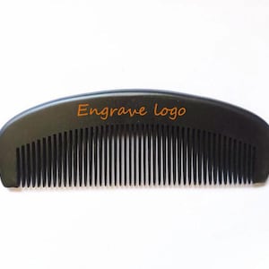Könnte beinhalten: Ein schwarzer Plastikkamm mit einem gebogenen Griff. Der Griff trägt den Text "Engrave logo".