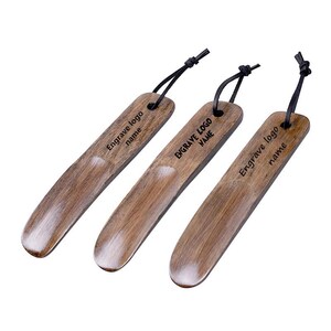 May include: Three wooden shoe horns with black leather straps. Each horn has the text "Engrave logo name" engraved on the surface.