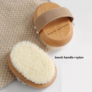 Op de afbeelding: Een houten lichaamsborstel met natuurlijke haren. De handgreep is gemaakt van beukenhout en heeft een bruin elastiek. De tekst "Engrave logo/name" is gegraveerd in de handgreep.
