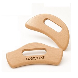 Puede incluir: Dos herramientas de madera de color claro con superficies lisas y curvas y aberturas integradas para el agarre. La herramienta inferior presenta el texto "LOGO/TEXT" impreso en color marrón oscuro en su parte frontal, mientras que la superior es lisa.