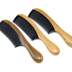 Puede incluir: Tres peines de madera con dientes negros están dispuestos sobre un fondo blanco. Los peines tienen un acabado de veta de madera natural en los mangos y un diseño curvo. Los dientes negros están muy juntos y los peines están ligeramente inclinados.