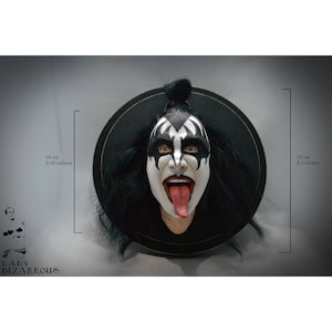 Puede incluir: Un busto pintado en blanco y negro de una persona con cabello negro largo y una lengua roja que sobresale. El busto está montado sobre una base circular negra. El busto mide 13,5 cm de alto y 8 cm de ancho.