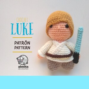 Puede incluir: Muñeco de Luke Skywalker tejido a crochet con una espada láser. El muñeco lleva una túnica blanca y pantalones marrones. El muñeco sostiene una espada láser azul. El texto "CROCHET - LUKE PATRÓN PATTERN" está en el fondo.