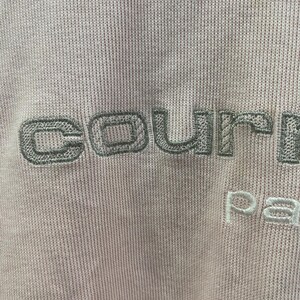 May include: Close-up of a light pink fabric with embroidered text. The word "courre" is stitched in a muted green, with "pa" in white below. The fabric has a ribbed texture.