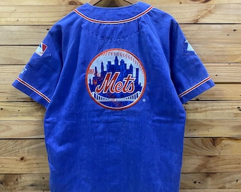 May include: A blue baseball jersey with the word "Mets" in a stylized design on the back. The design includes a cityscape and a baseball. The jersey has red and white trim.