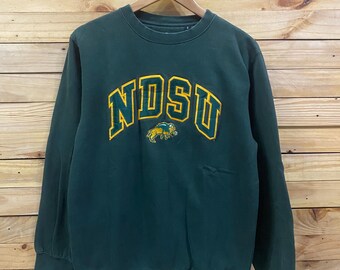 May include: A dark green crewneck sweatshirt featuring the letters NDSU in yellow and green embroidered lettering across the chest, accompanied by a small embroidered yellow and green bison graphic positioned directly below the text.