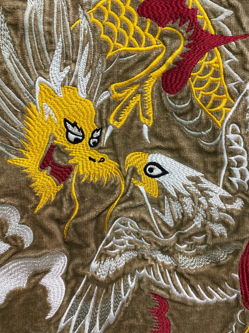 Pu&ograve; includere: Disegno ricamato con un drago giallo con accenti rossi e un'aquila bianca con ali grigie su uno sfondo di tessuto marrone.