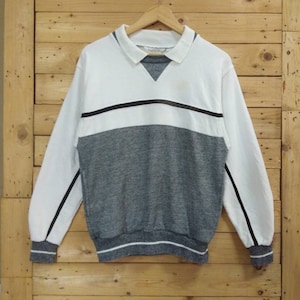Può includere: Un maglione a maniche lunghe bianco e grigio con una striscia nera sul petto e bordi neri sulle maniche. Il maglione ha un colletto.