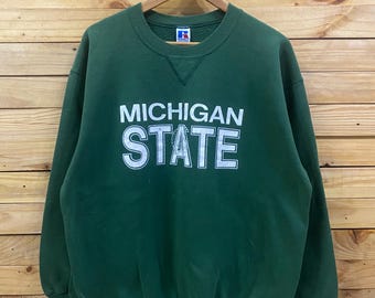 May include: Green sweatshirt with the words "MICHIGAN STATE" in white block letters. The sweatshirt has a crew neck and long sleeves. The brand logo is visible on the upper back and lower left side.