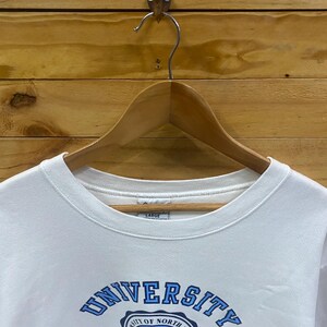 K&ouml;nnte beinhalten: Wei&szlig;es Sweatshirt mit Rundhalsausschnitt und dem blauen Schriftzug "UNIVERSITY OF NORTH CAROLINA". Das Sweatshirt hat eine Schildgrafik mit den W&ouml;rtern "CHAPEL HILL" und "LVX". Das Gr&ouml;&szlig;enetikett lautet "LARGE".