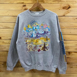 May include: A gray sweatshirt with a colorful graphic print of Disneyland park attractions. The print includes the text "Disneyland Resort" and "Discover the Magic".