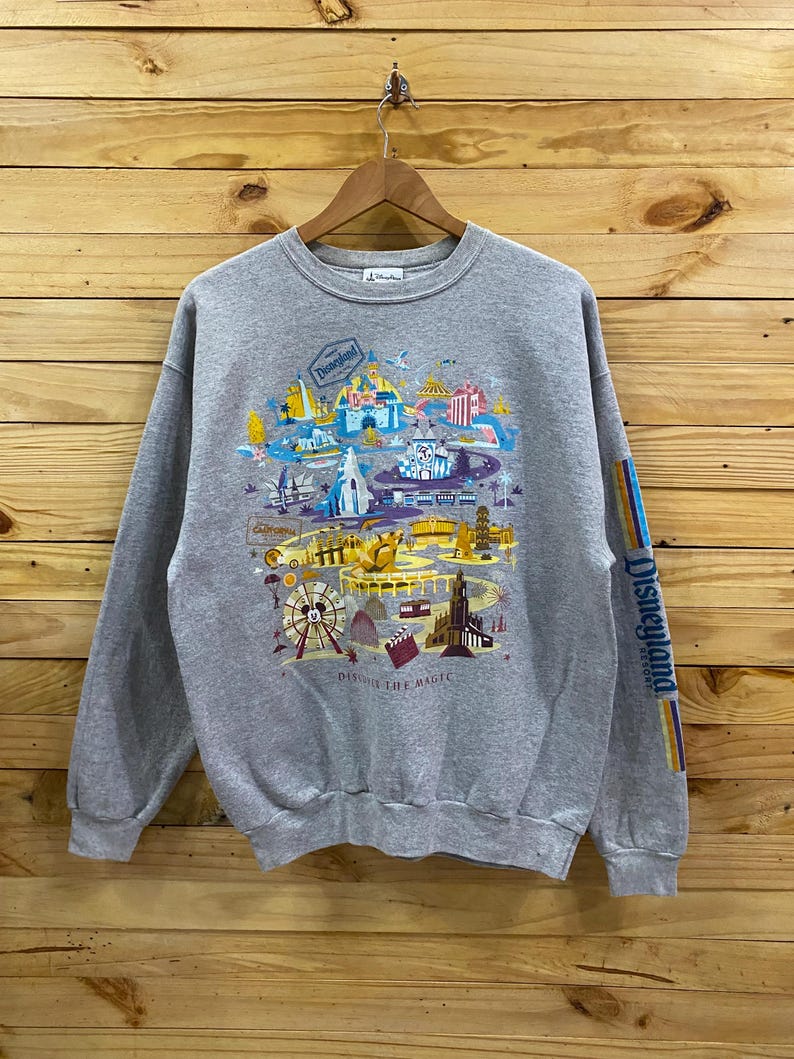 May include: A gray sweatshirt with a colorful graphic print of Disneyland park attractions. The print includes the text "Disneyland Resort" and "Discover the Magic".