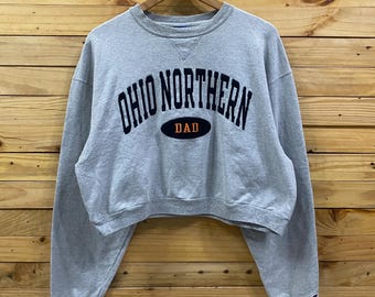May include: A gray cropped sweatshirt with long sleeves, featuring the text "OHIO NORTHERN" in navy blue arched lettering above an oval with the word "DAD" in orange. The sweatshirt is hanging on a wooden hanger.
