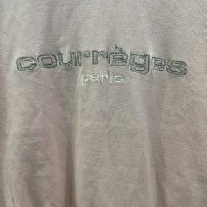 May include: Pale pink sweatshirt with the embroidered text "courr&egrave;ges paris" in a darker gray color. The fabric has a ribbed texture, and the stitching is visible.