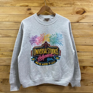 Może przedstawiać: Szara bluza z vintage'owym logo Universal Studios Hollywood z fajerwerkami i tekstem "EST. 1915 USA WE'VE SCENE IT ALL!"