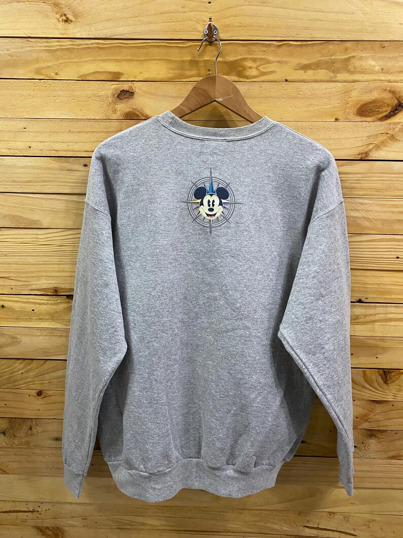 May include: A gray sweatshirt with a Mickey Mouse graphic on the back. The graphic features Mickey Mouse wearing a blue hat and a compass with a yellow, blue, and red design.