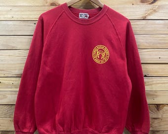 May include: A red long-sleeve crewneck sweatshirt featuring a yellow circular graphic on the chest. The graphic contains the text "GOTEMBA KOZAK RIDING CLUB SINCE 1971" surrounding a horseshoe icon. The sweatshirt has ribbed cuffs and a ribbed hem.
