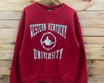 May include: A red crewneck sweatshirt with the words "WESTERN KENTUCKY UNIVERSITY" in white block letters. The university's logo is centered below the words "WESTERN KENTUCKY". The sweatshirt is hanging on a wooden hanger against a wooden background.