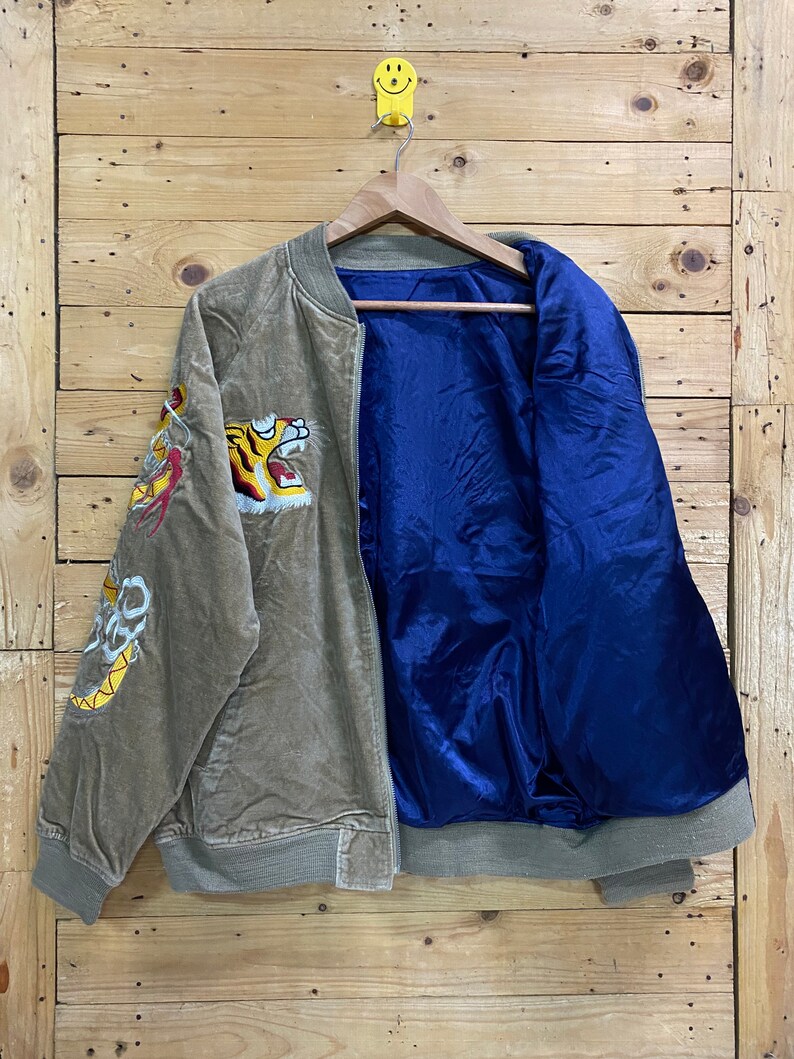 Pu&ograve; includere: Una giacca bomber in velluto a coste marrone con fodera in raso blu. La giacca presenta ricami di tigre e drago sulle maniche.