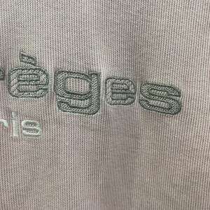 May include: Close-up of a light purple knit fabric with embroidered text. The text, in a muted green, reads "&eacute;eges" above "ris". The fabric has a ribbed texture, and the embroidery adds a subtle contrast in color and texture.