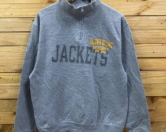 May include: A heather gray quarter-zip sweatshirt featuring the text JACKETS in large dark gray letters and BALDWIN WALLACE UNIVERSITY EST. 1845 in yellow text on the chest. The garment has a stand-up collar with a silver zipper pull.
