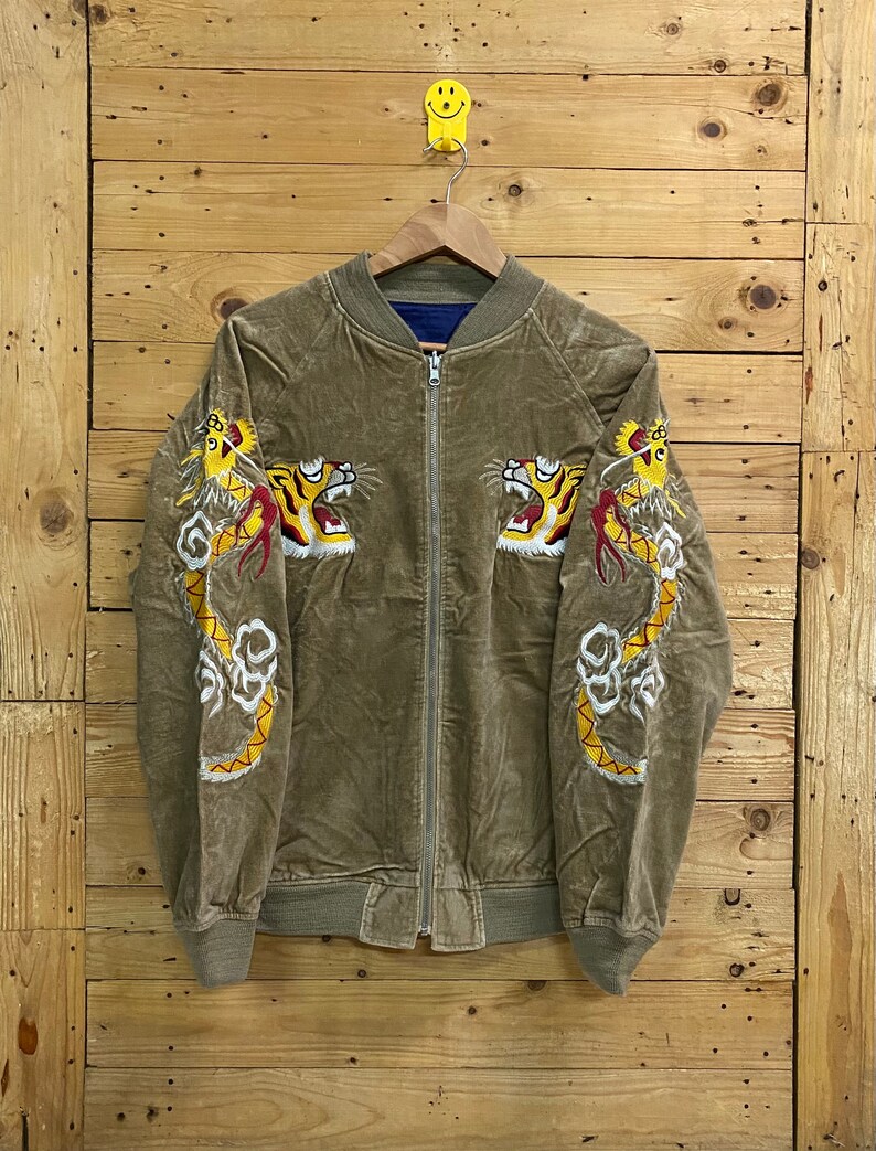 Pu&ograve; includere: Una giacca bomber in velluto a coste marrone con draghi gialli ricamati sulle maniche e una chiusura a zip.