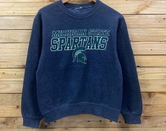 May include: Dark blue sweatshirt with the words "MICHIGAN STATE SPARTANS" in green and white lettering. A green Spartan helmet logo is below the text. The sweatshirt is hanging on a wooden hanger.
