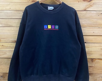 May include: A black long-sleeve crewneck sweatshirt featuring a FILA brand tag at the collar. The chest displays four colorful square icons above the text FILA MAD SOUND CONDITIONING in red, yellow, purple, and blue, all centered on the front.