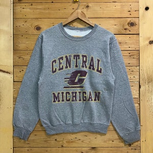 Pode incluir: Camisola de moletom cinza com uma estampa gráfica vintage de "CENTRAL MICHIGAN" em letras amarelas e bordô. O gráfico inclui uma letra "C" estilizada com um raio bordô.