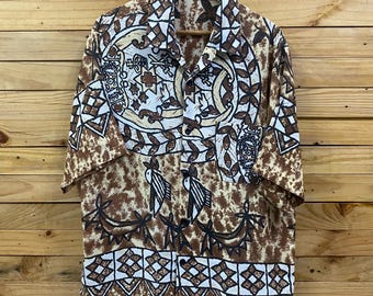 May include: A short-sleeved button-down shirt with a brown and cream-colored pattern. The shirt features a repeating design of geometric shapes, floral elements, and bird-like figures. The shirt is hanging on a wooden hanger against a wooden background.