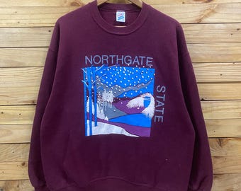 May include: A maroon crewneck sweatshirt featuring a graphic print of a snowy landscape with trees and mountains. The text NORTHGATE is printed above the graphic, and the word STATE is printed vertically along the right side of the graphic.
