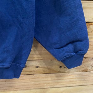 May include: Close-up of a blue sweatshirt sleeve. The sleeve is made of a soft, textured fabric and has a ribbed cuff. The background is a light brown wooden surface.