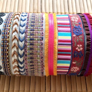 Peut inclure: Une collection de rubans et de galons colorés et à motifs, comprenant du cuir noir, de la dentelle noire, du tissu tissé et du ruban à carreaux.