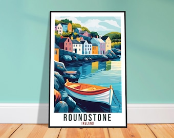 May include: A framed art print of Roundstone, Ireland. The image features colorful buildings along a bay, a small boat, and the text "ROUNDSTONE IRELAND". The artwork is in a stylized, illustrative style, with a black frame and a wooden floor.