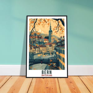 May include: A framed art print of Bern, Switzerland, featuring a watercolor-style illustration of the city. The artwork showcases buildings, a river, and a church with a tall steeple, all under a warm, autumnal sky. The word "BERN" is printed at the bottom.